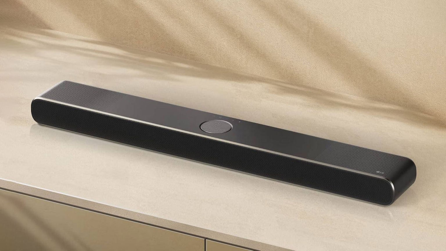 : Un’elegante soundbar LG di colore nero, collocata su una superficie beige, caratterizzata da un design minimalista, spigoli arrotondati e griglie perforate su entrambe le estremità.