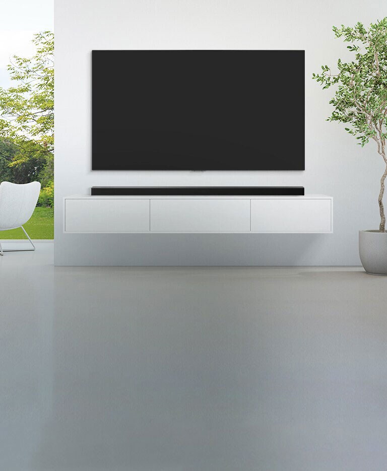 Un TV e una soundbar sono collocati in un grande soggiorno bianco e da un’ampia finestra si vede una foresta lussureggiante. 