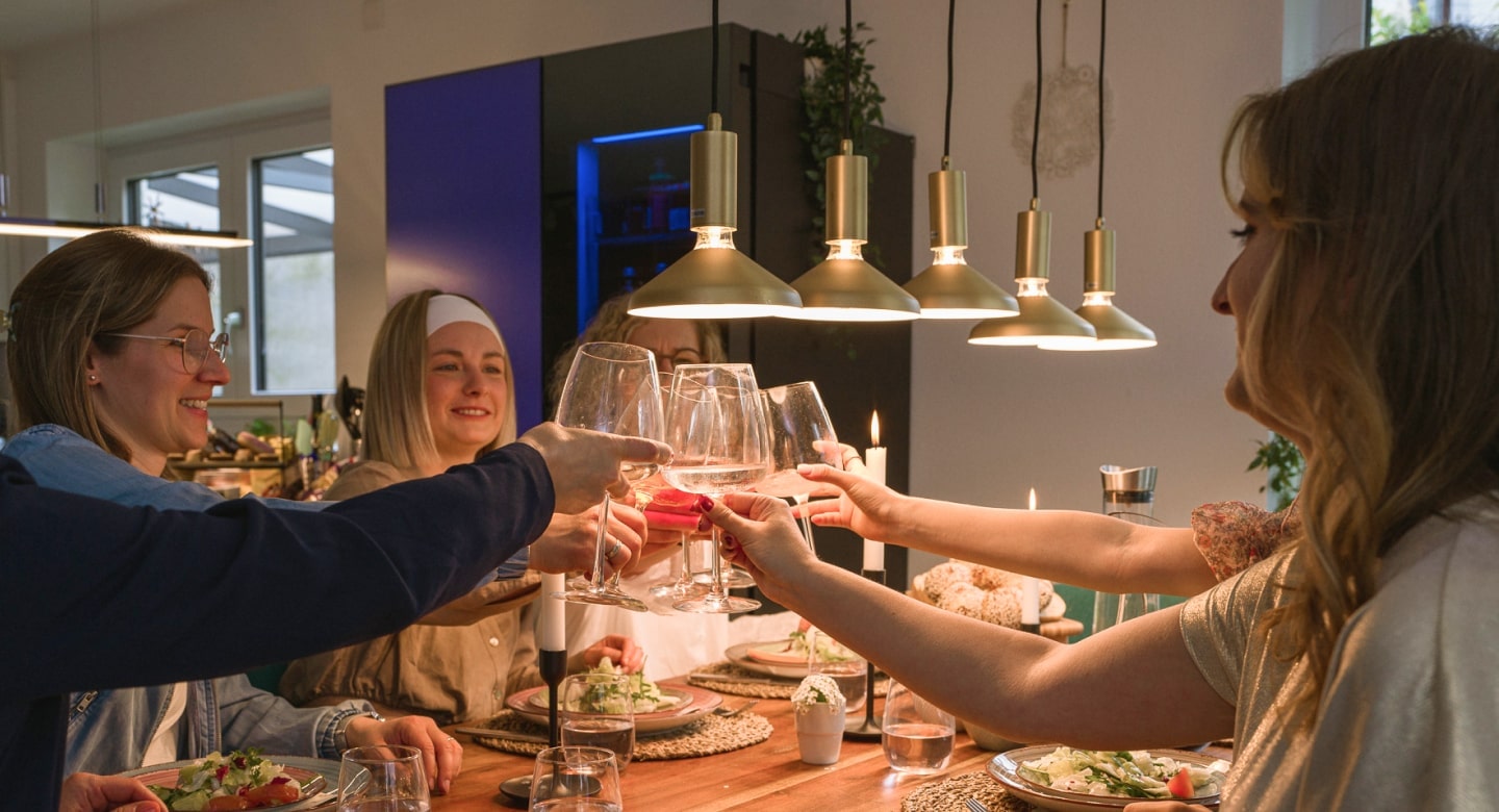 Le persone brindano al tavolo da pranzo davanti al LG MoodUP Refrigerator, i cui colori migliorano l'atmosfera della festa.