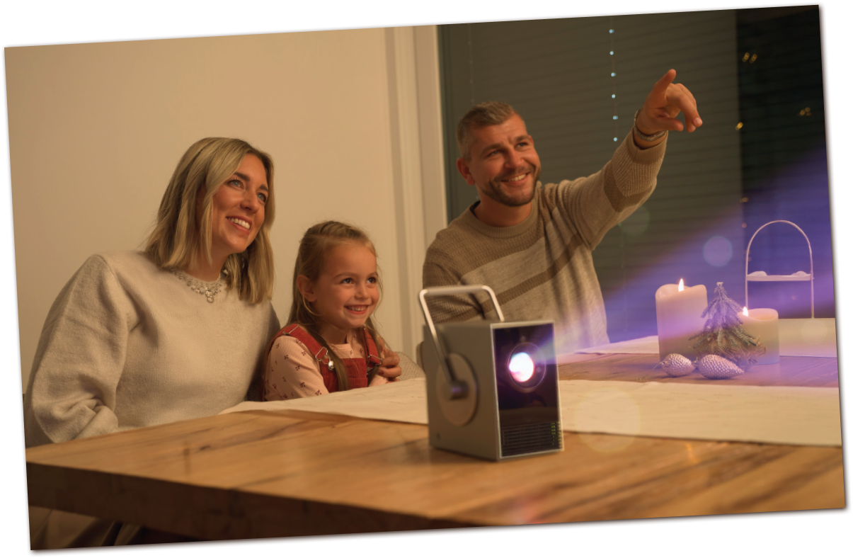 Famiglia che festeggia Natale con LG CineBeam Q sul tavolo. Una coppia e un bambino sorridono in un'atmosfera calda e festiva.