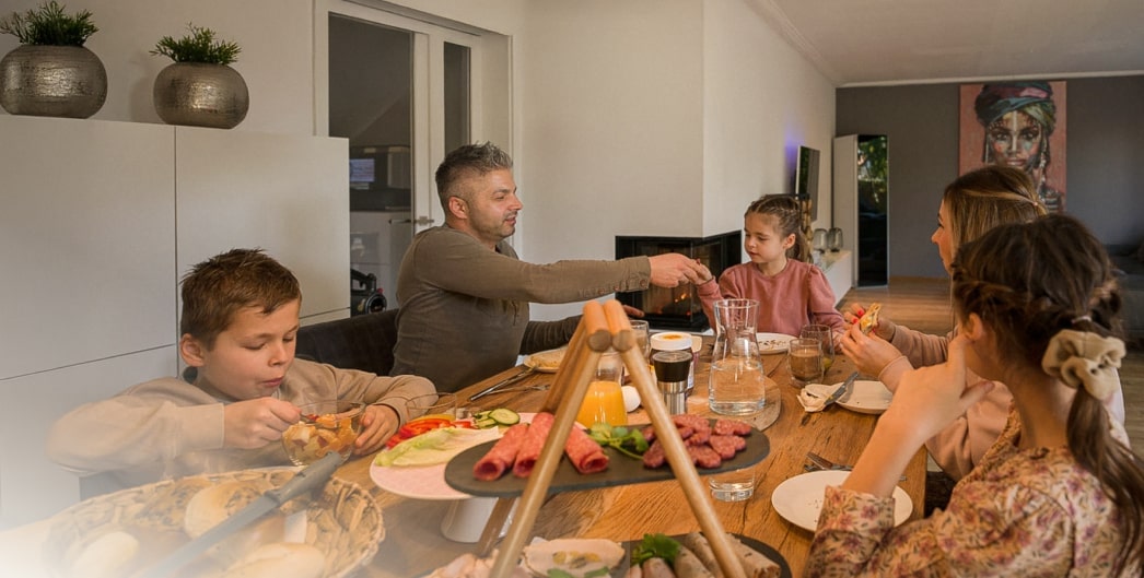 Una famiglia di cinque persone che cena insieme a un tavolo, creando momenti speciali con cibo e conversazioni in un ambiente accogliente.