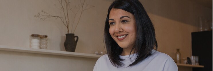 Donna che versa il tè in una teiera in una cucina moderna, sorridente e serena.