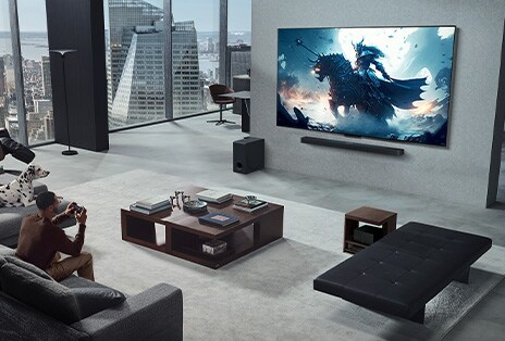 壁掛けのLGトゥルーワイヤレスTVとLG Soundbarでビデオゲームをしている人がいるリビングルーム。手にコントローラを握りっているが、ゲーミングコンソールはすぐに見えない。これらも目に見える配線がありません。Zero Connect Boxがサイドテーブルの下にしまわれ、ほとんど見えない。