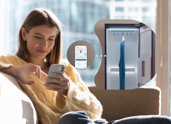 LG Stylerが動作している間、スマートフォンを手にしてソファに座る女性