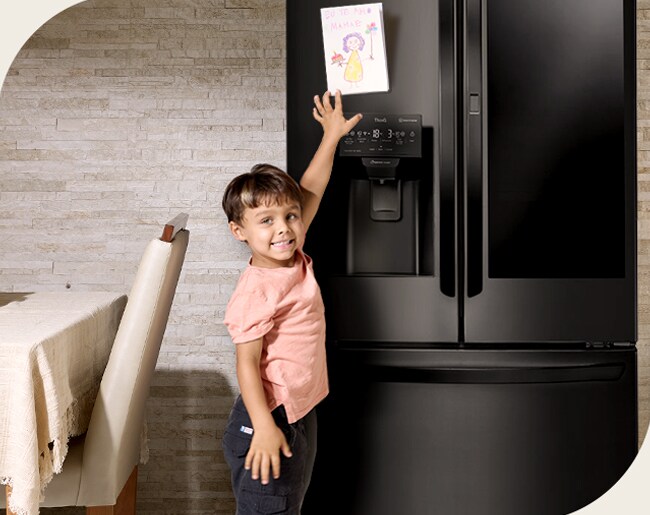 Un niño coloca un dibujo de una flor y un pastel en la puerta del refrigerador; la mamá sonríe al encontrar flores reales escondidas dentro.		