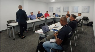 Personas en una sala de reuniones, escuchando a un presentador de pie frente a la mesa en forma de U, en el Nuevo Centro de Negocios LG de Latinoamérica.