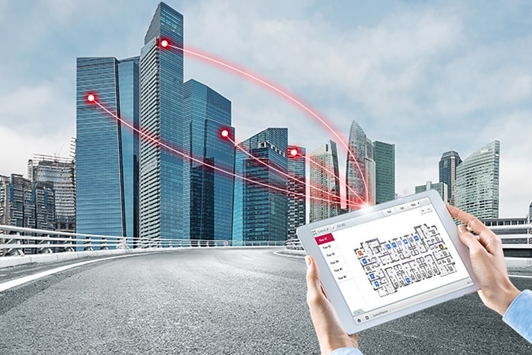 Una persona sostiene una tableta que muestra una solución de control. Cuatro líneas rojas se extienden desde la tableta y se conectan a edificios a la izquierda.