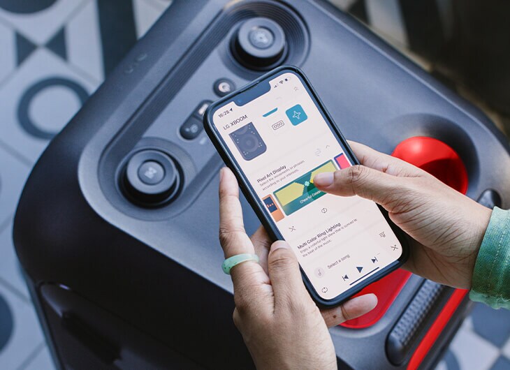 Primer plano de la bocina LG XBOOM con una persona usando la aplicación Thinq en su smartphone para controlar la música y la iluminación.