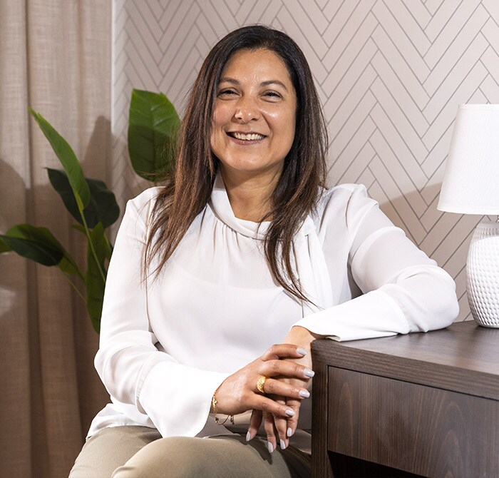 Rosana sonriendo con los brazos sobre el escritorio, vistiendo una camisa blanca.