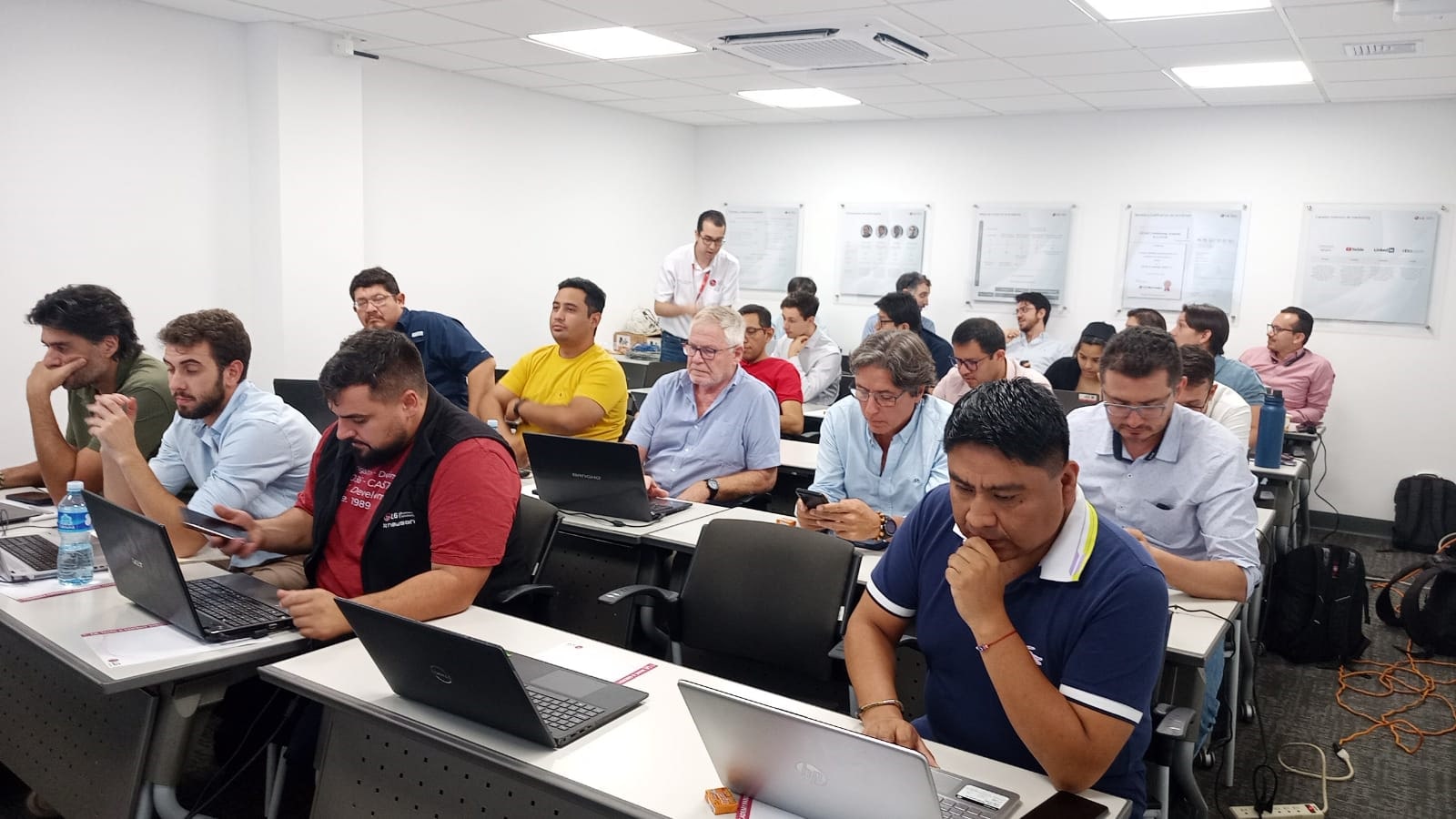 Grupo de personas en una sala de capacitación, trabajando en laptops y escuchando al instructor, en el Primer Foro LG de Soluciones de Automatización y Controles 2023.