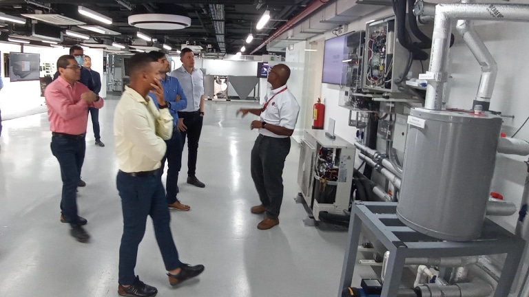 Grupo de hombres en una sala técnica, observando una explicación sobre un equipo industrial en el Colombia HVAC Annual Meeting.