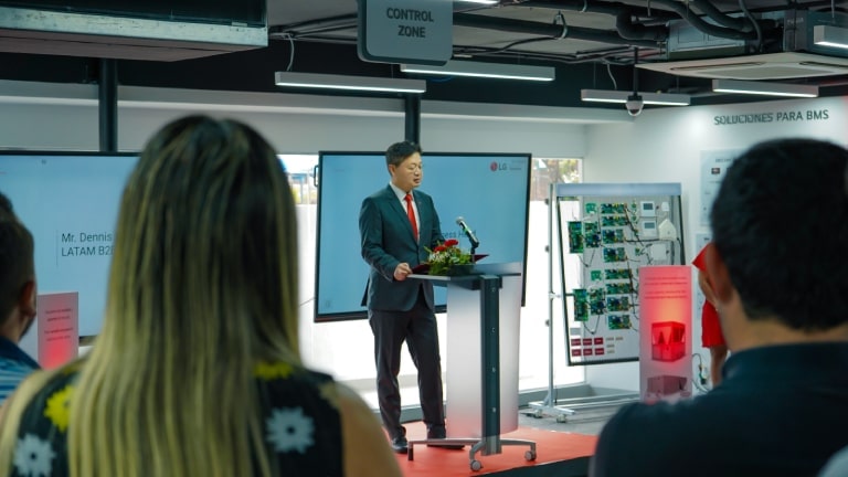 Hombre en traje presentando en una sala técnica del Nuevo Centro de Soluciones de Negocios para Latinoamérica, con la audiencia atenta al frente.