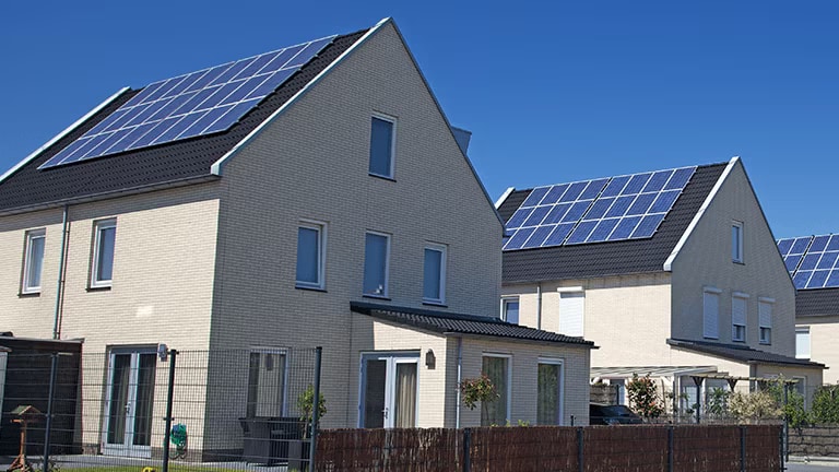 La vista frontal de las casas de tono de marfil se exhibe lado a lado con el techo negro cubierto con paneles solares.