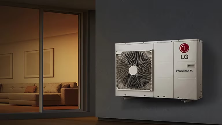 La unidad LG Therma V se coloca en la pared derecha, mientras que un salón luminoso con un sofá largo se puede ver a través de las ventanas de vidrio a la izquierda.