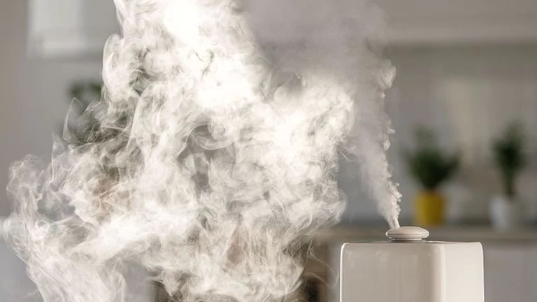 Humidificador liberando una gran cantidad de vapor en un espacio interior, con un fondo ligeramente desenfocado.