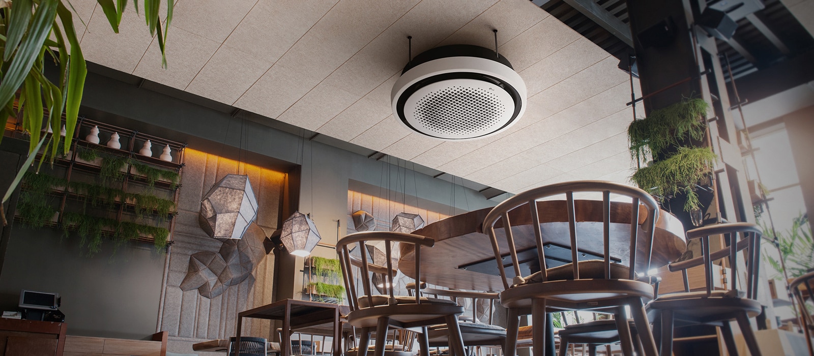 Desde la perspectiva de una hormiga, se despliega una cafetería adornada con sillas, mesas y plantas, mientras en el techo se despliega un casete redondo LG.