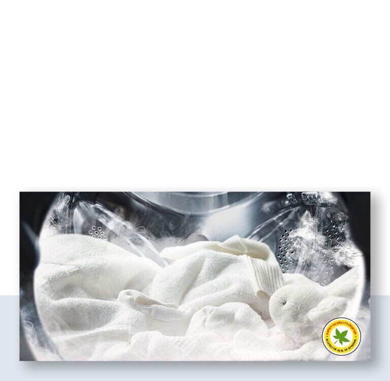 Un suave albornoz blanco y un peluche se muestran con vapor dentro del tambor de la lavadora.