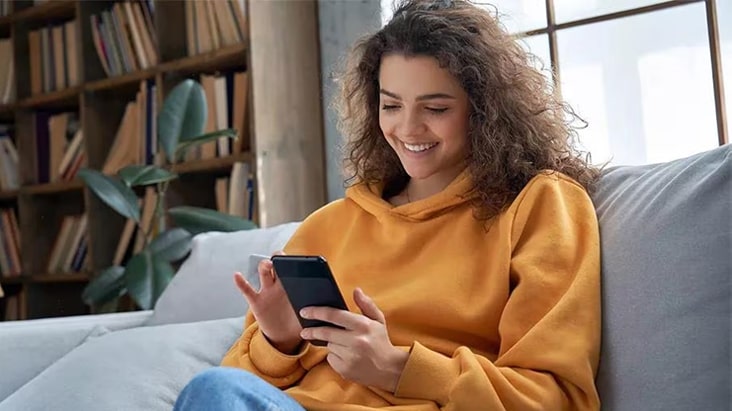 La mujer esta sentada en el sillón y utiliza su celular