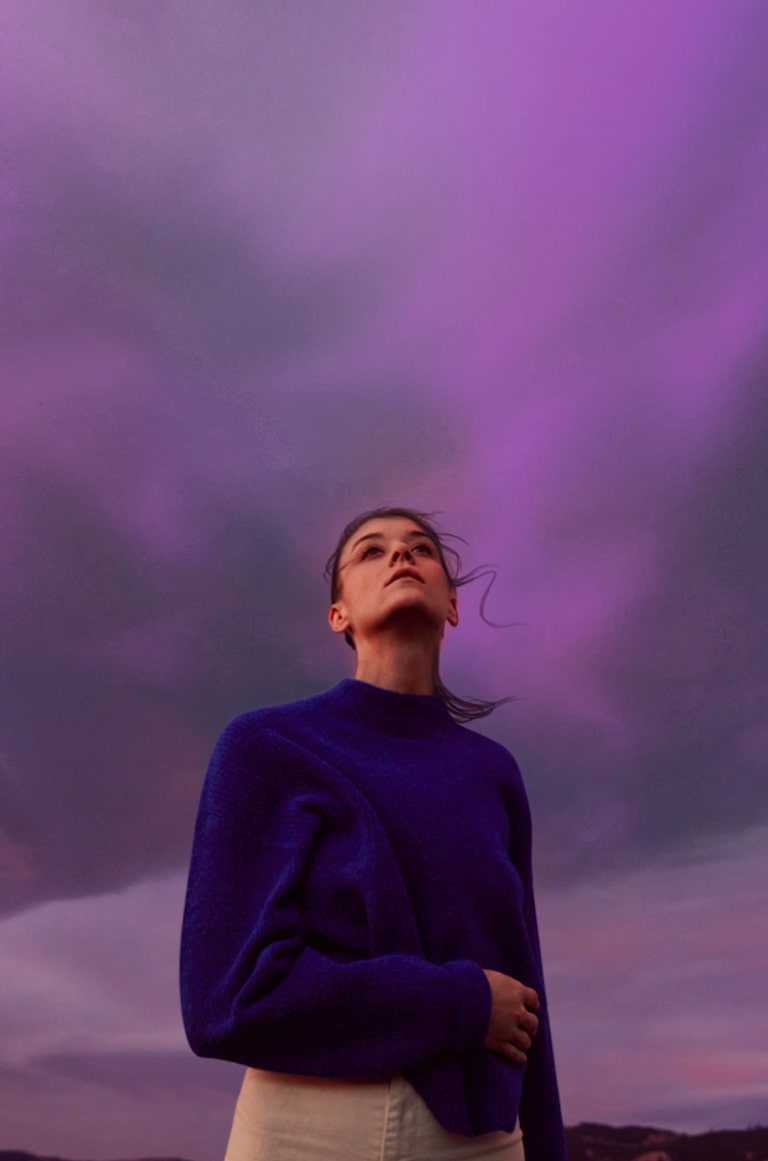 Una mujer mira un cielo morado. Su cabello se sacude ligeramente.