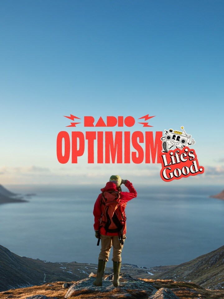 Una mujer con una chaqueta de senderismo roja está de pie en un lugar donde se puede ver el vasto océano y montañas cubiertas de nieve. La imagen también presenta el logotipo del eslogan "Radio Optimism" y el logotipo de "Life's Good." junto a la mujer.