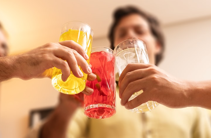 Tres amigos brindando con copas de bebidas en la fiesta. Bebida amarilla, roja, blanca con hielo.