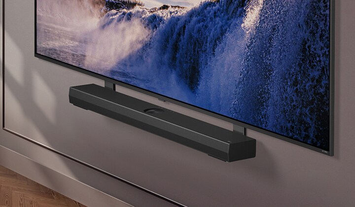 El soporte Synergy se muestra con una LG QNED TV. El soporte Synergy y la LG QNED TV se unen mientras se realiza una panorámica hacia abajo para mostrar la parte inferior de la televisión. Aparece la LG Soundbar colocada en el soporte Synergy. El fondo aparece con la pared.