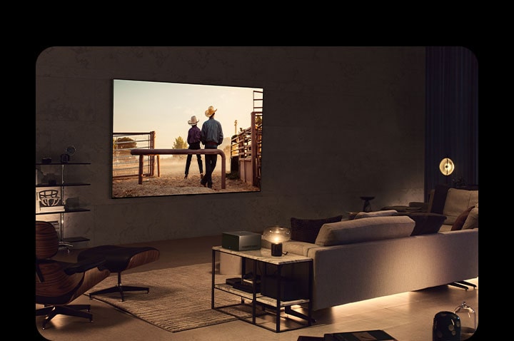 A man watching a cowboy movie with his dog in a cozy living space in the evening. There are no wires surrounding the wall-mounted LG OLED TV, and the Wireless Connect Box sits neatly on a side table.