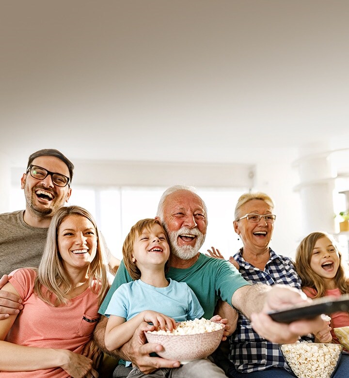 A family sits laughing while the grandfather points the remote outward.