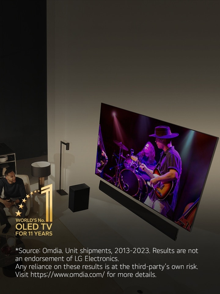 An overhead perspective of a man and woman watching a concert on a large OLED TV in a modern apartment.