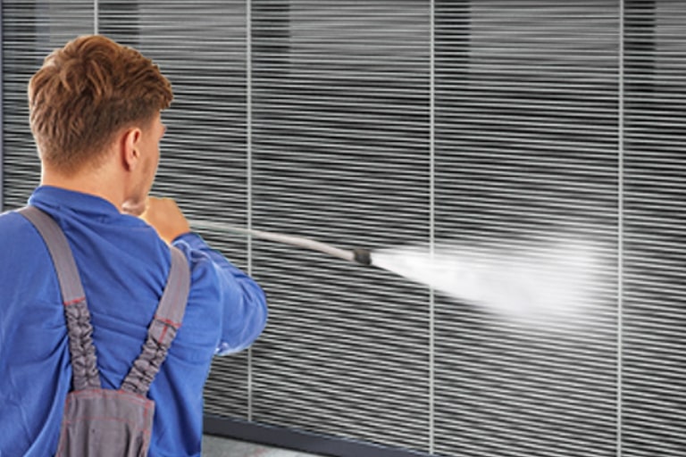 A man in a blue shirt is holding a water hose and cleaning the large filter of LG Inverter Single Package.