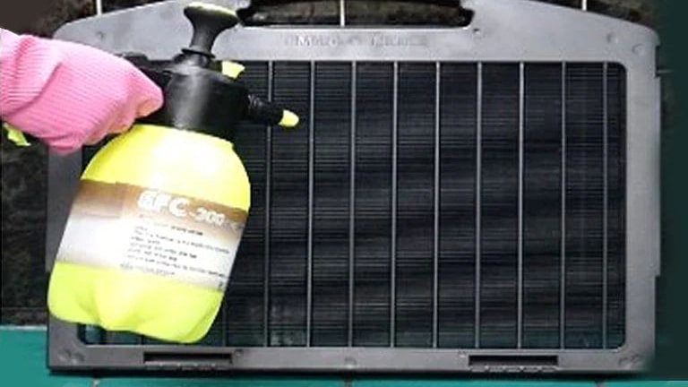 Garbed in gloves, a person expertly wields a weeding sprayer, applying water to a black, rectangular air purification filter.