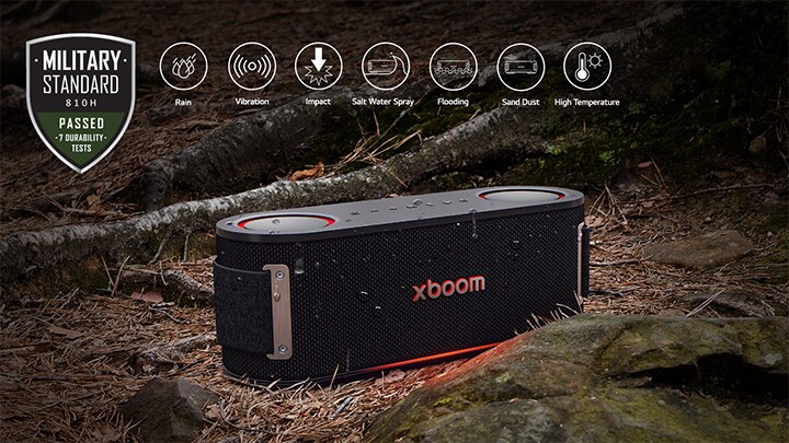 xboom Bounce is placed on soil covered with wet leaves, between a tree root and a stone. On the above left side Military standard logo is placed.	