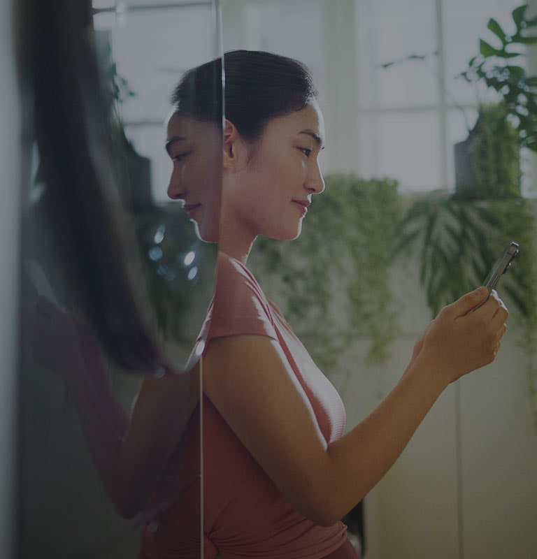 Image shows a woman standing next to a washtower, looking into her phone while smiling.