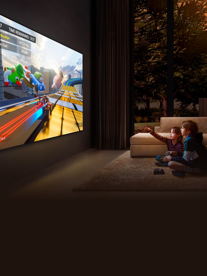 Een zijaanzicht van een ultragrote LG TV gemonteerd op een muur in een gezellige woonkamer met een kleurrijke game in beeld. Twee kinderen zitten op de grond voor de televisie en hebben gamecontrollers in de hand.