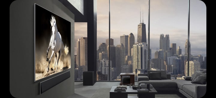 Exclusief penthouse. De skyline van de stad is zichtbaar door de ramen van de woonkamer die van de vloer tot het plafond reiken. LG True Wireless TV en LG Soundbar worden aan de muur bevestigd. De inrichting van de ruimte is heel geraffineerd en opgeruimd. De Zero Connect Box is nauwelijks te zien onder een van de bijzettafeltjes.