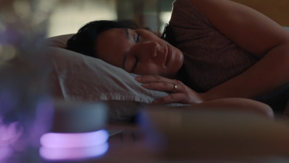 Een vrouw ligt op haar zij in bed te slapen. Voor haar licht het LG ThinQ ON apparaat op. Het gordijn gaat open en een man aait een hond. De vrouw die op haar zij lag wordt wakker.