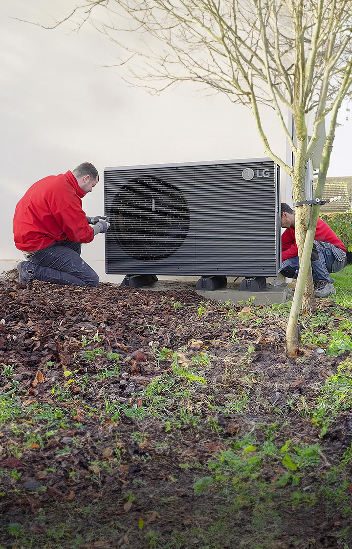 Twee installateurs met rode jumpers installeren de LG warmtepomp THERMA V R290 Monobloc in de achtertuin van het huis.