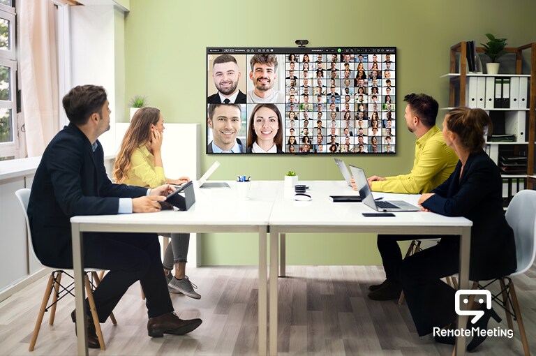 Vier mensen zitten in een vergaderruimte tv te kijken en houden een teleconferentie. Het scherm toont de mensen die aan de vergadering deelnemen.