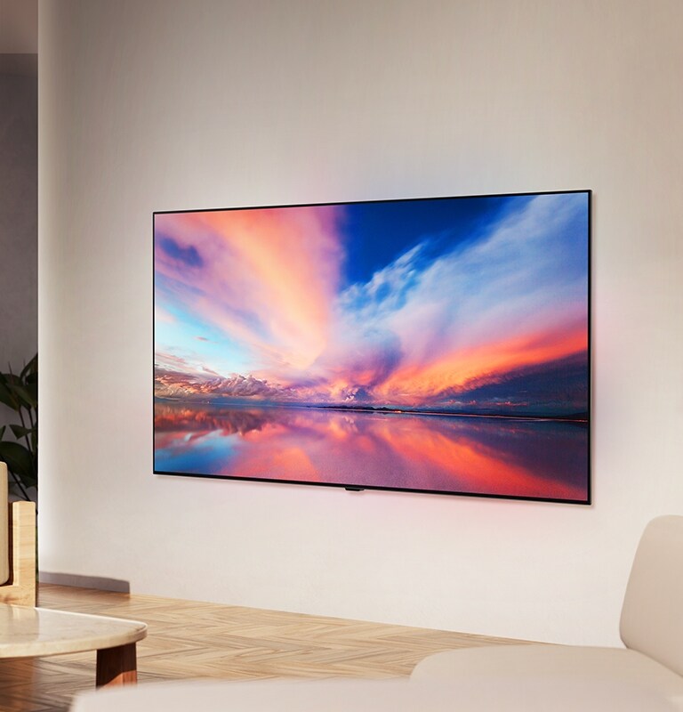 LG OLED TV, OLED B4 op de muur van een neutrale woonruimte met een kleurrijke foto van een zonsondergang over een oceaan op het scherm.