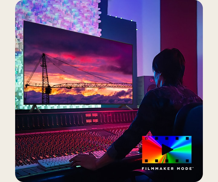 Een man in een donkere bewerkingsstudio die naar een LG-tv kijkt die de zonsondergang weergeeft. Rechtsonder in de afbeelding staat een FILMMAKER Mode-logo.