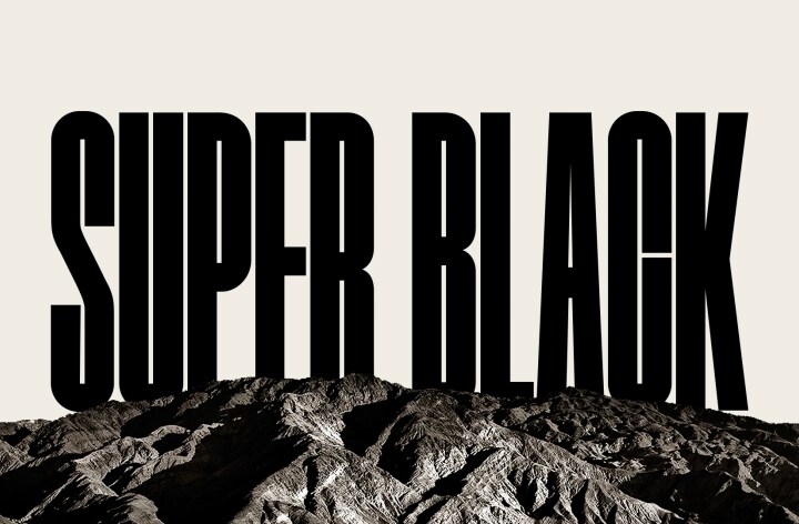 Se abre un vídeo con las palabras "SUPER BLACK" en mayúsculas negras y en negrita. Una escena montañosa negra con una definición nítida se eleva para cubrir las letras, revelando también un pueblo y dunas de arena. La copia negra desaparece detrás de un cielo negro.