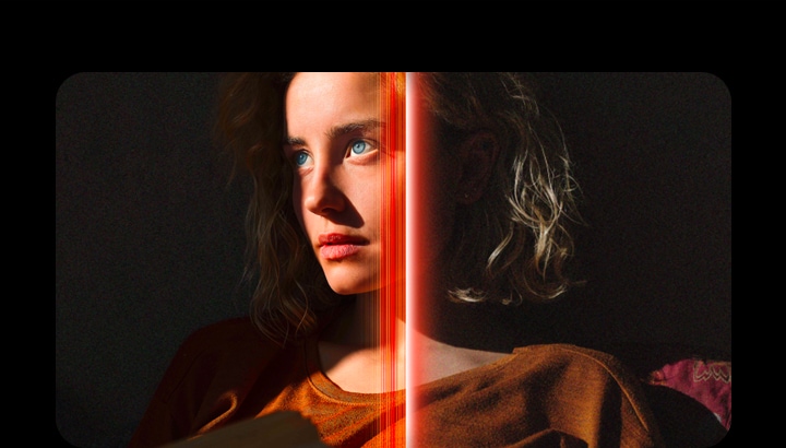 Una mujer con penetrantes ojos azules y un top naranja quemado en un espacio oscuro. Las líneas rojas que representan los refinamientos de la IA cubren parte de su rostro, que es brillante y detallado, mientras que el resto de la imagen parece menos colorido.