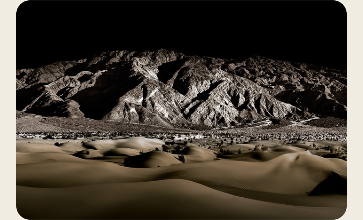 Las palabras 'PERFECT BLACK' en blanco sobre fondo negro. Una cadena montañosa rocosa bien iluminada aparece al frente, luego se mueve hacia arriba para revelar el paisaje de abajo mientras las palabras 'PERFECT BLACK' se desvanecen.