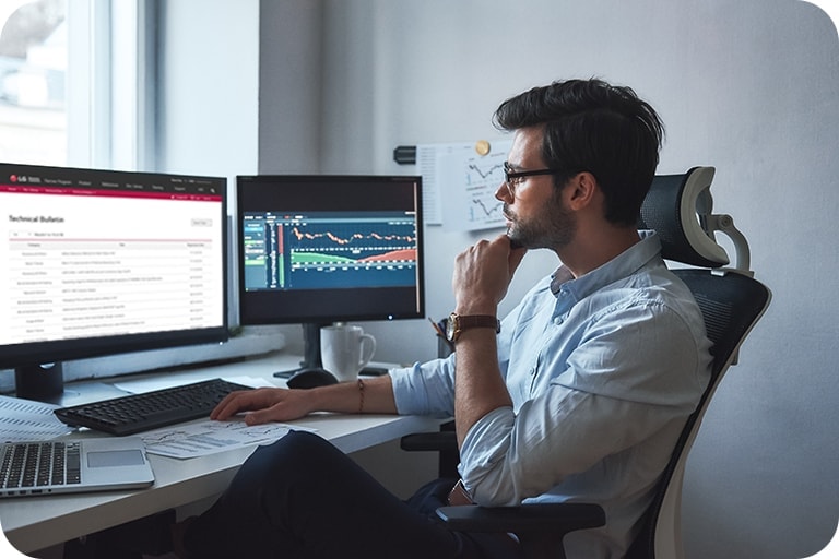 A man is observing dual monitors, with a list displayed on one screen and a graph on the other.