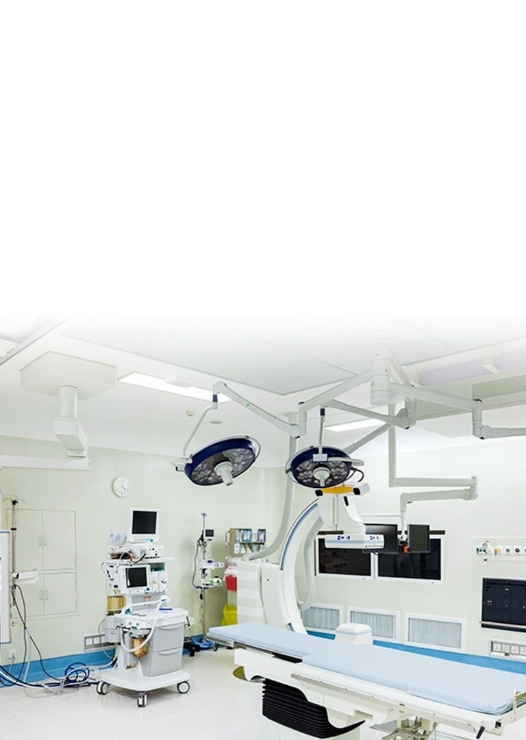 An operating room with white walls featuring patient's bed, multiple medical devices connected via electric cables and monitors with black screen.