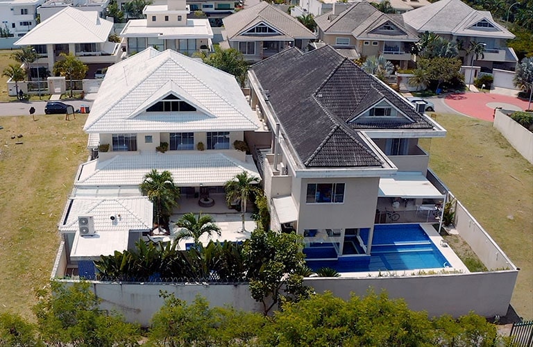 A luxury residence building with a white roof on the left half and a black roof on the right half. Both residences boast a backyard pool.