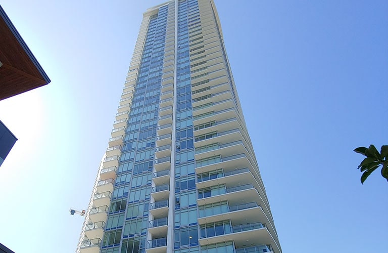 The glass-clad high-rise condos with the balcony shoot up in the blue sky. 