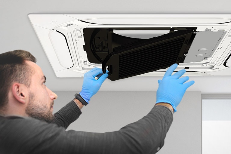 A man wearing blue nitrile gloves is replacing the black filter in an installed LG Ceiling-mounted Cassette.