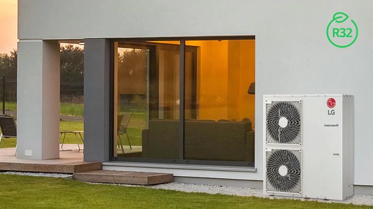 An LG Therma V Monobloc graces the right exterior of a white-toned house, a couch glimpsed through the left glass window.