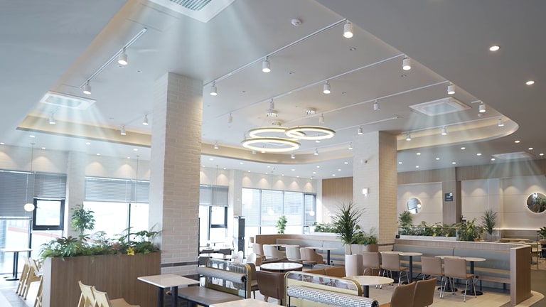 Three ceiling units disperse visible airflow in the large white-tone restaurant, while central lights cast a space.